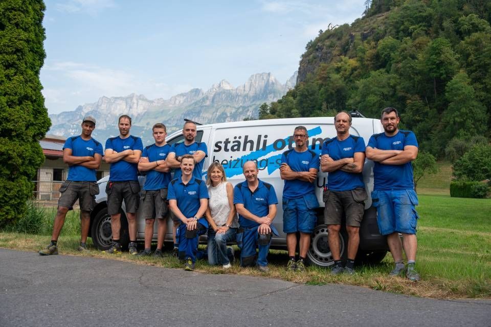 Eine Gruppe von Menschen in blauen Hemden posiert vor einem Strassenschild mit Bergen im Hintergrund.