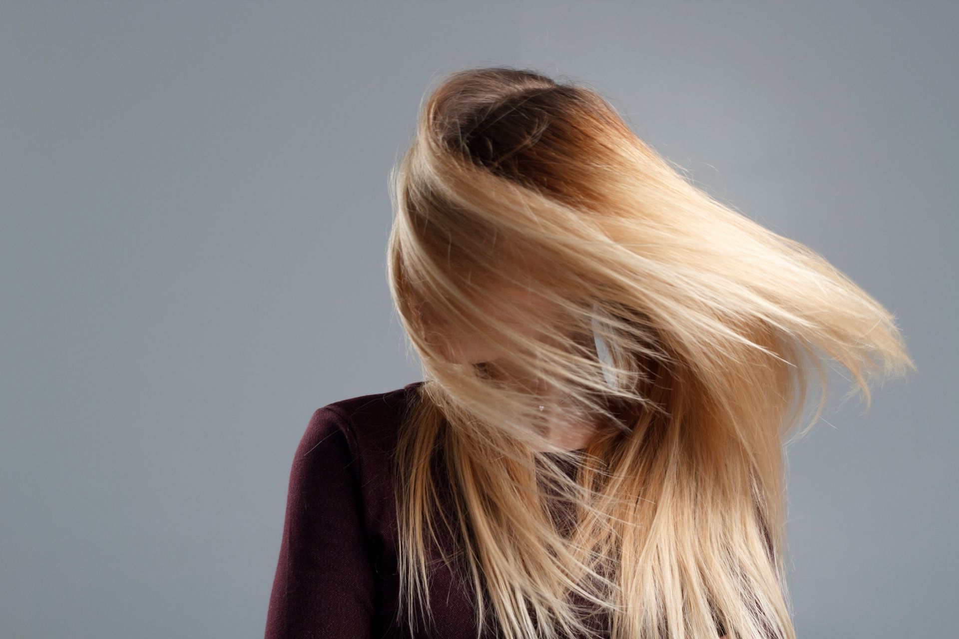 Una mujer con cabello largo y rubio se cubre la cara con su cabello.