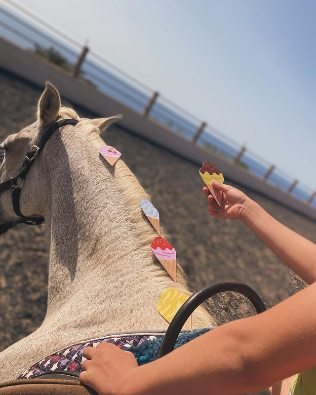 Una persona decora la crin de un caballo con conos de helado de papel de colores. El caballo está afuera