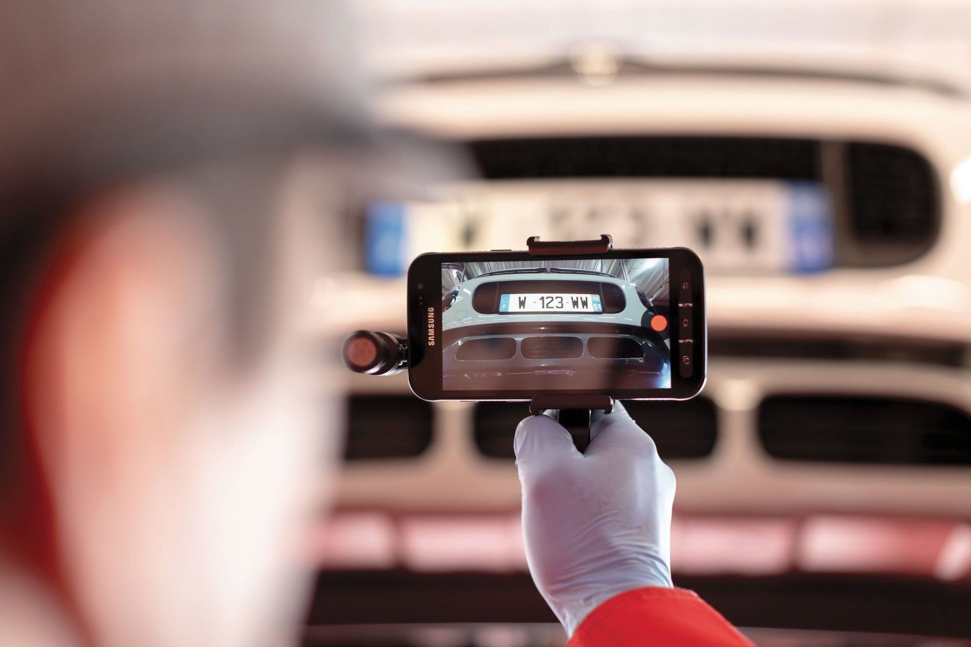Une personne utilise un smartphone pour photographier la plaque d'immatriculation d'une voiture dans un garage.