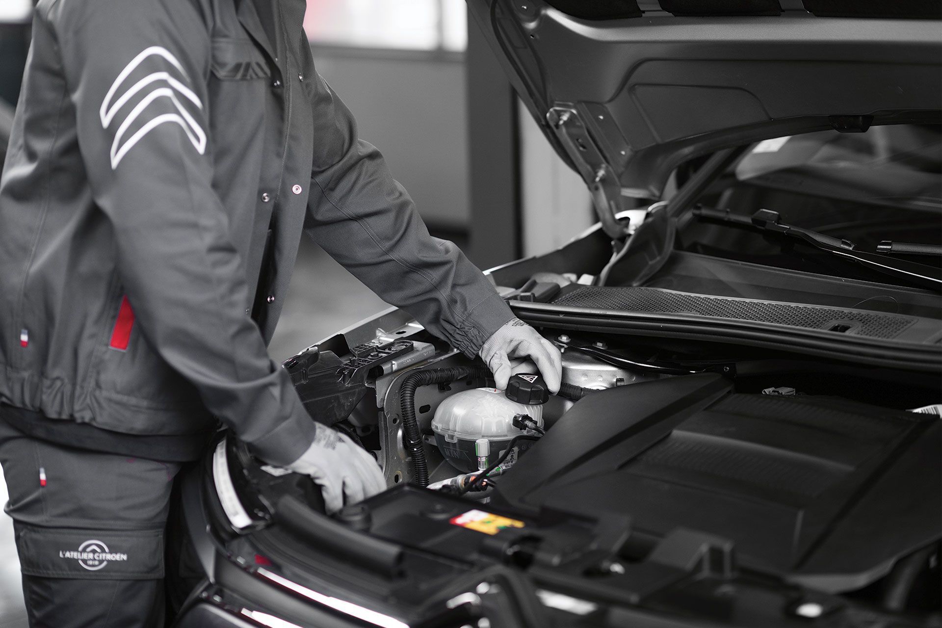 Un mécanicien en uniforme vérifie le moteur d'une voiture dans un garage.