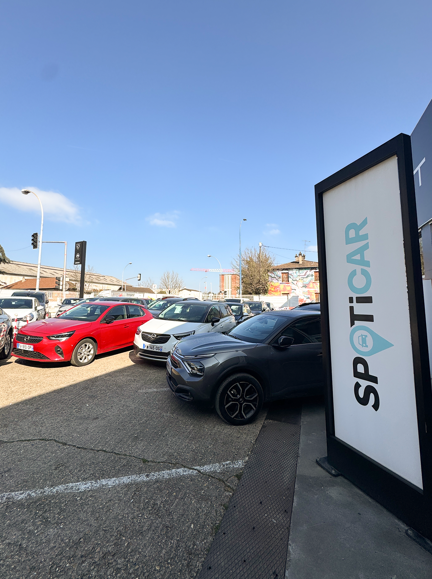 Voitures garées devant un panneau Spoticar par une journée ensoleillée.