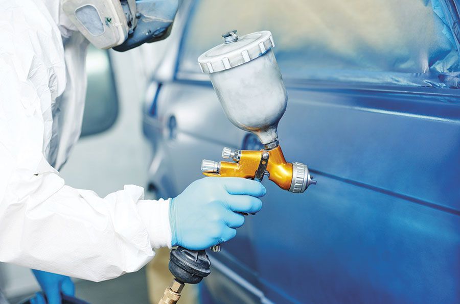 Une personne portant un équipement de protection peint une voiture bleue au pistolet à peinture.
