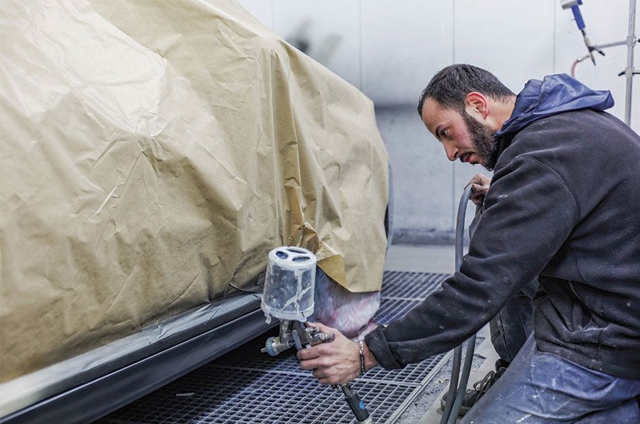 Une personne peignant le panneau latéral d'une voiture à l'aide d'un pistolet à peinture dans une cabine de peinture.