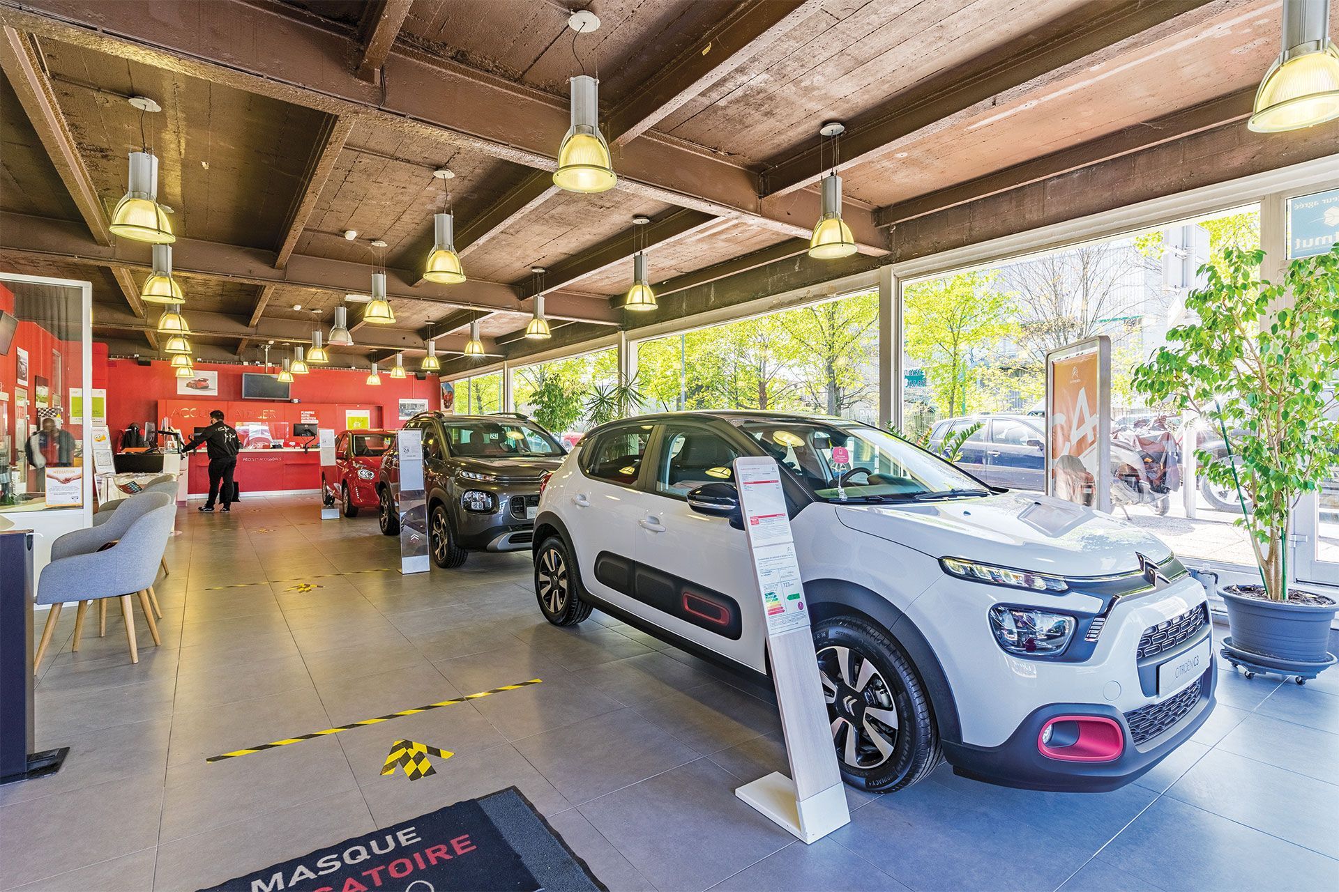 Intérieur d'un showroom automobile avec une voiture blanche au premier plan, d'autres voitures et du personnel à l'arrière-plan.