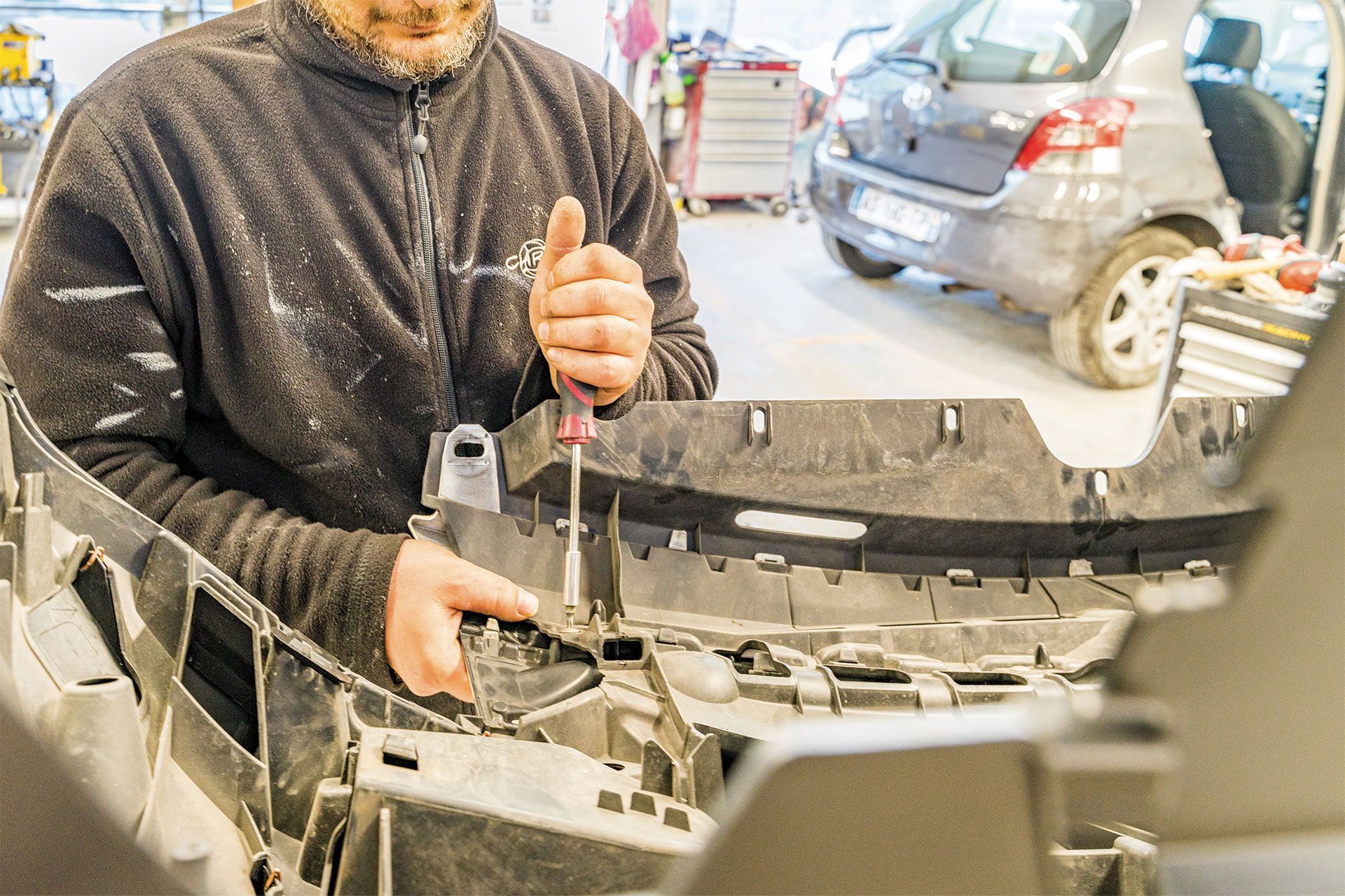Un mécanicien utilise un tournevis sur le pare-chocs d'une voiture dans un atelier.