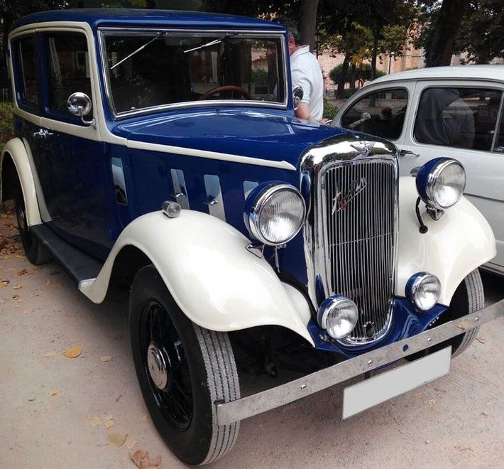 Un coche azul y blanco está aparcado al lado de un coche blanco.