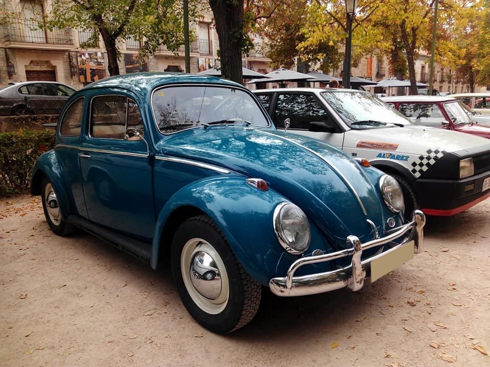 Un escarabajo azul está estacionado junto a un coche blanco.