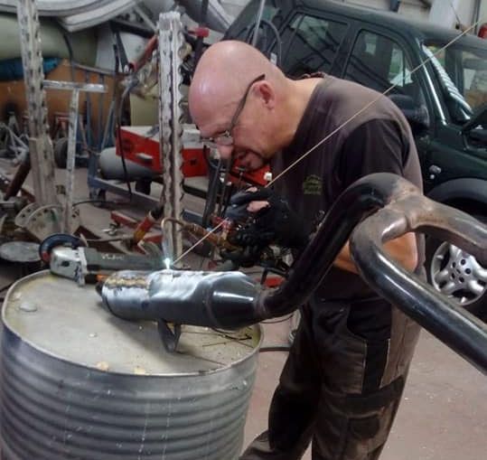Un hombre con gafas está soldando una tubería en un garaje.