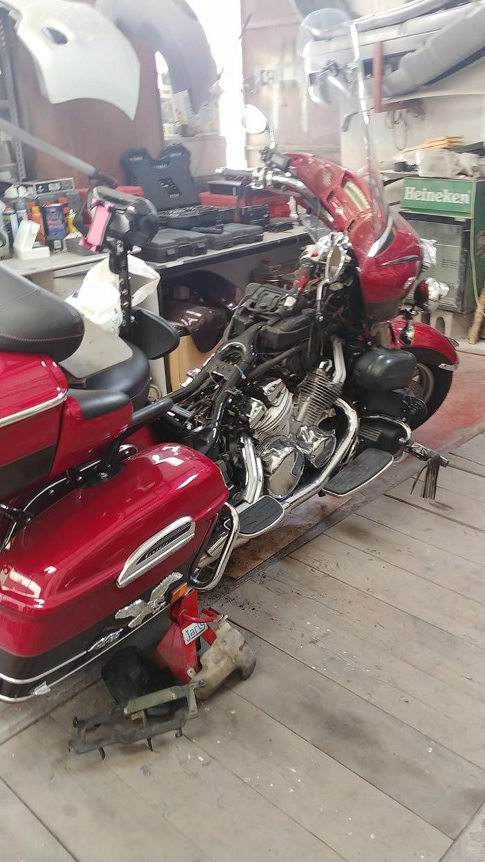 Una motocicleta roja está parada sobre un piso de madera en un garaje.