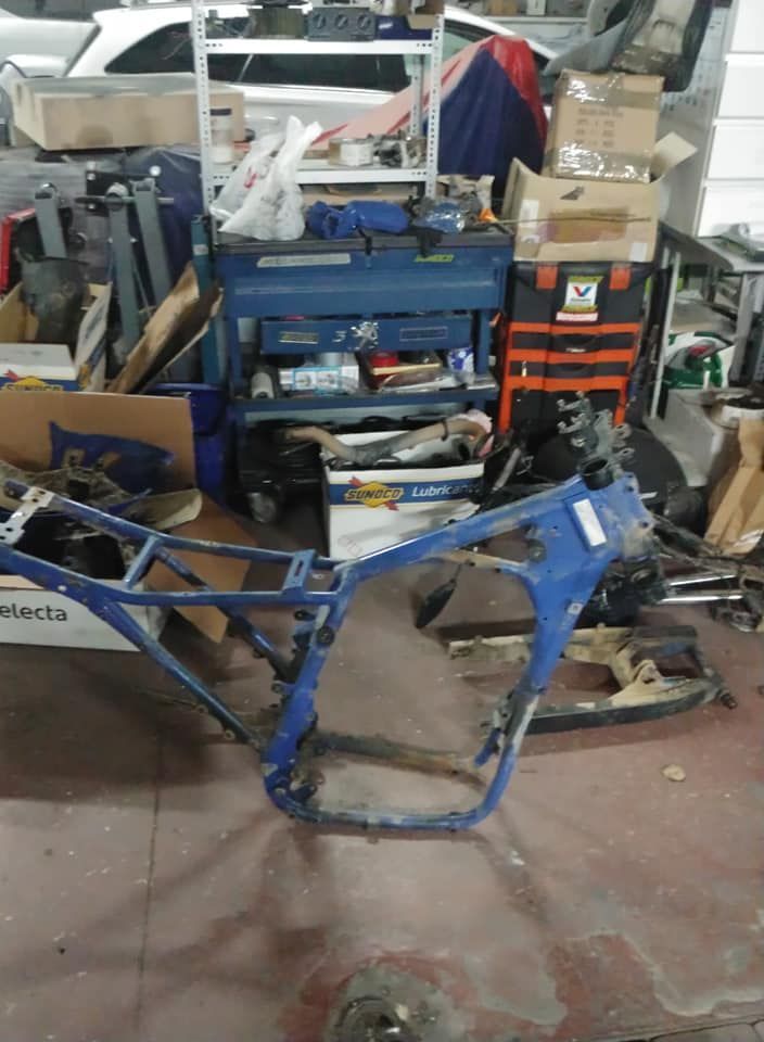 Un cuadro de motocicleta azul está estacionado en un garaje desordenado.