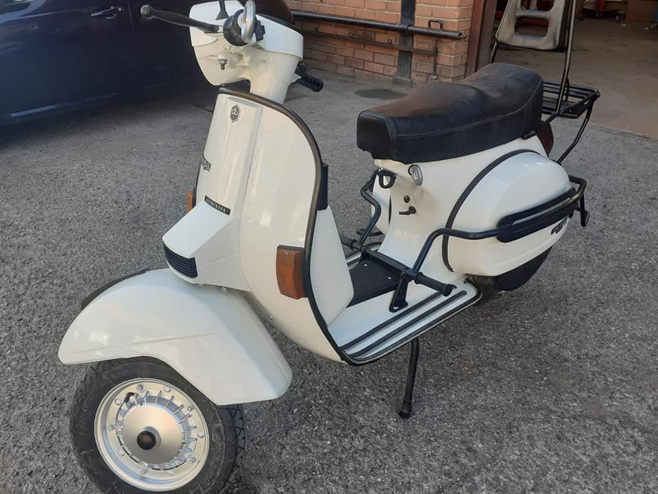 Un scooter blanco está estacionado en un estacionamiento al lado de un automóvil.