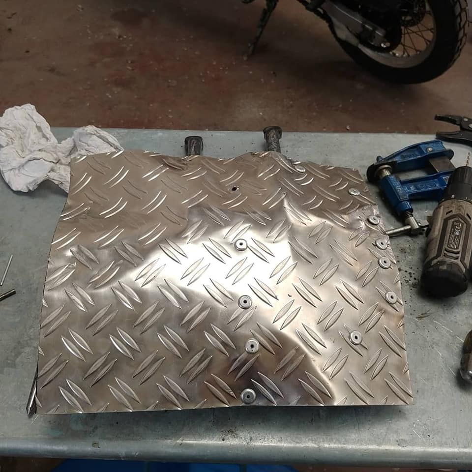 Un trozo de metal está sobre una mesa junto a herramientas y una motocicleta.