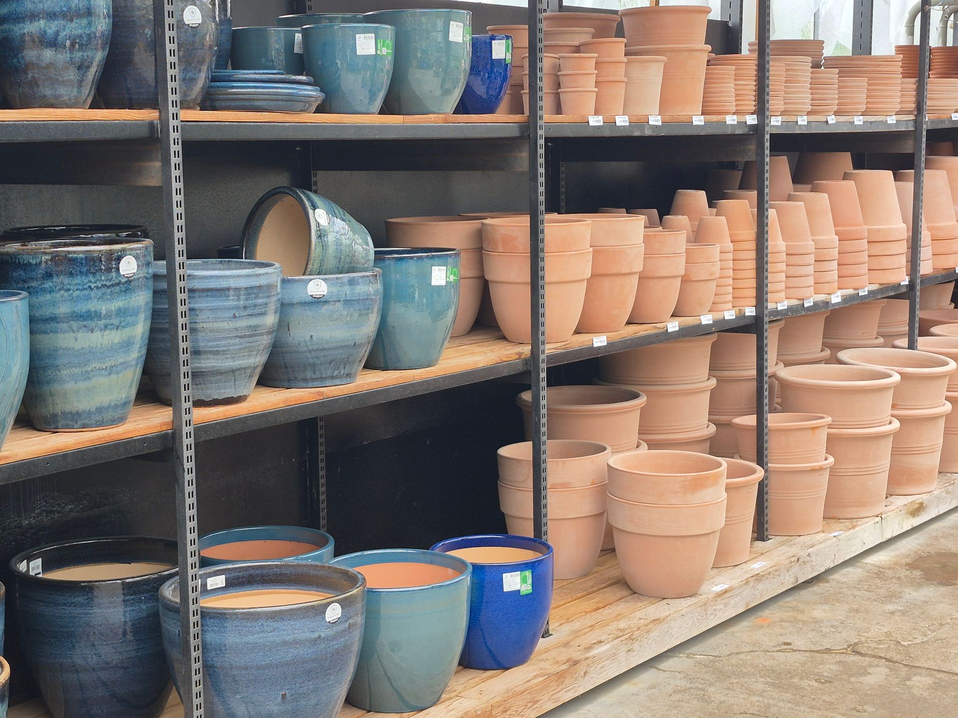 Des étagères dans un magasin présentent divers pots de fleurs en céramique et en terre cuite de différentes tailles et nuances de bleu et de beige.
