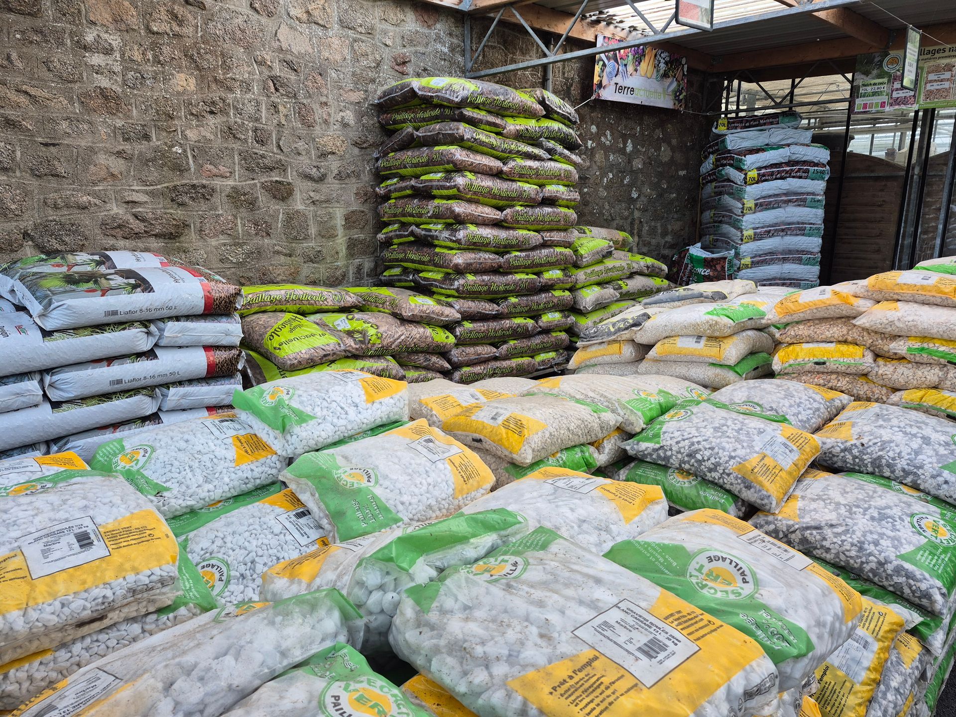 Une allée de magasin montrant des piles de roches et de pierres d'aménagement paysager en sacs, adossées à un mur de pierre.