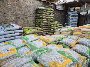 Des sacs de gravier et de terre sont empilés contre un mur de pierre dans une jardinerie.