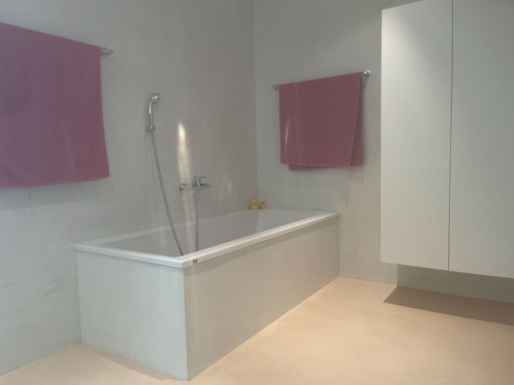 Ein modernes Badezimmer mit weißer Badewanne, Handbrause und zwei rosa Handtüchern an der Wand.