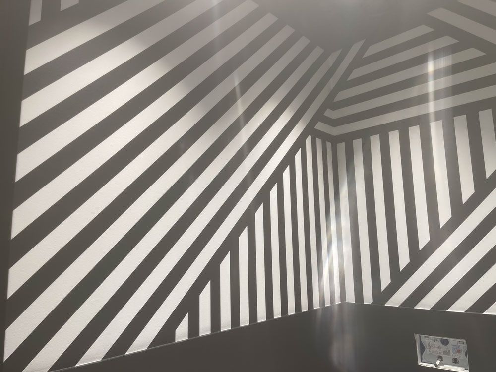 Wände, die mit einem geometrischen Muster aus dicken schwarzen und weißen diagonalen und vertikalen Streifen bemalt sind, die sich an den Eckkanten treffen.