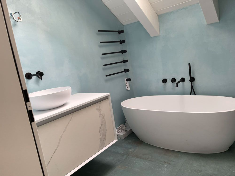 Ein modernes Badezimmer mit hellblauen Wänden, einem weißen Steinwaschtisch, einer freistehenden weißen Badewanne und mattschwarzen Armaturen.