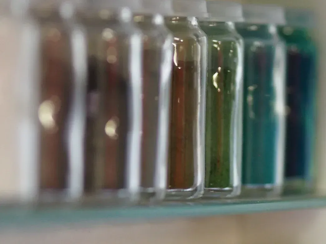 Auf einem Regal stehen mehrere Flaschen mit verschiedenfarbigen Flüssigkeiten.