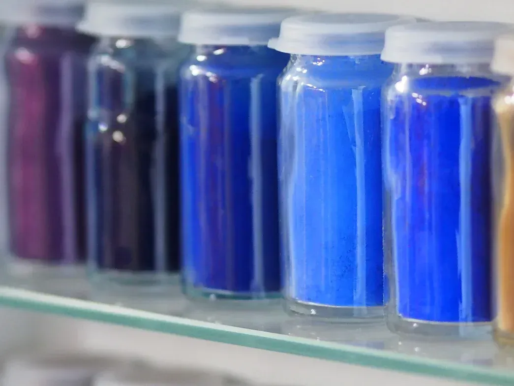 Auf einem Glasregal stehen eine Reihe blauer und violetter Flaschen.