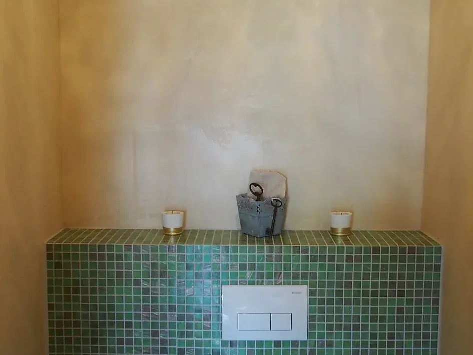 Ein Badezimmer mit grünen Fliesen und einem weißen Spülknopf.