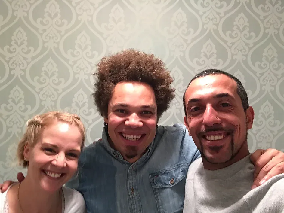 Drei Personen posieren für ein Foto vor einer gemusterten Wand