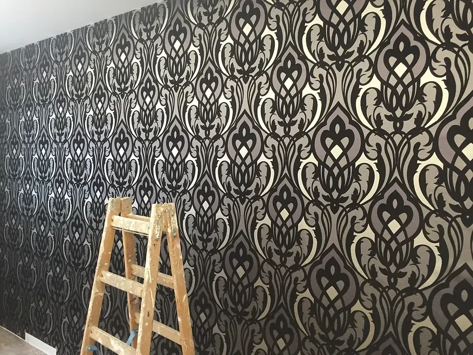 Vor einer Wand mit gemusterter Tapete steht eine Holzleiter.