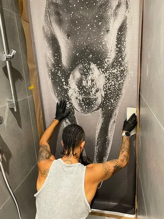 Ein Mann reinigt in einem Badezimmer einen Duschvorhang mit einem Schwamm.