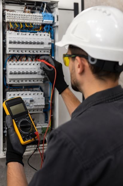 Técnico probando un panel eléctrico con un multímetro, usando casco y gafas de seguridad.