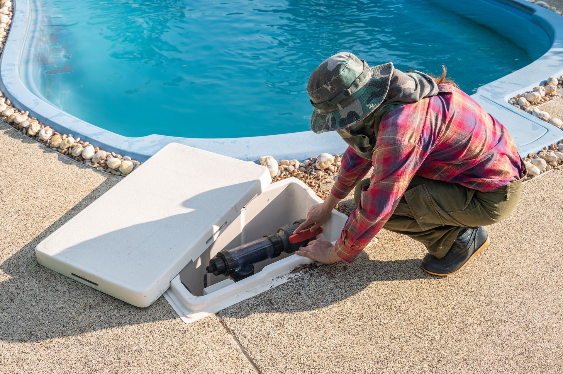 Un techicien ouvre une boîte blanche près d'une piscine et accède à l'équipement qui s'y trouve.
