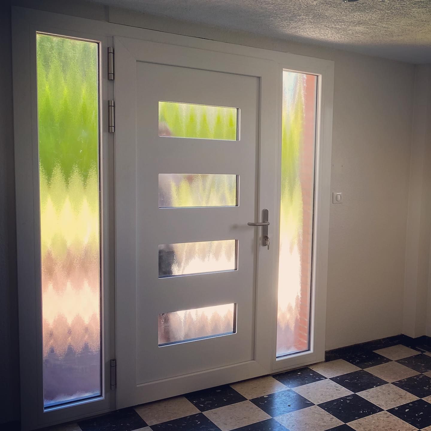 Une porte d'entrée vu de l'intérieur avec deux grandes vitres sur les côtés.