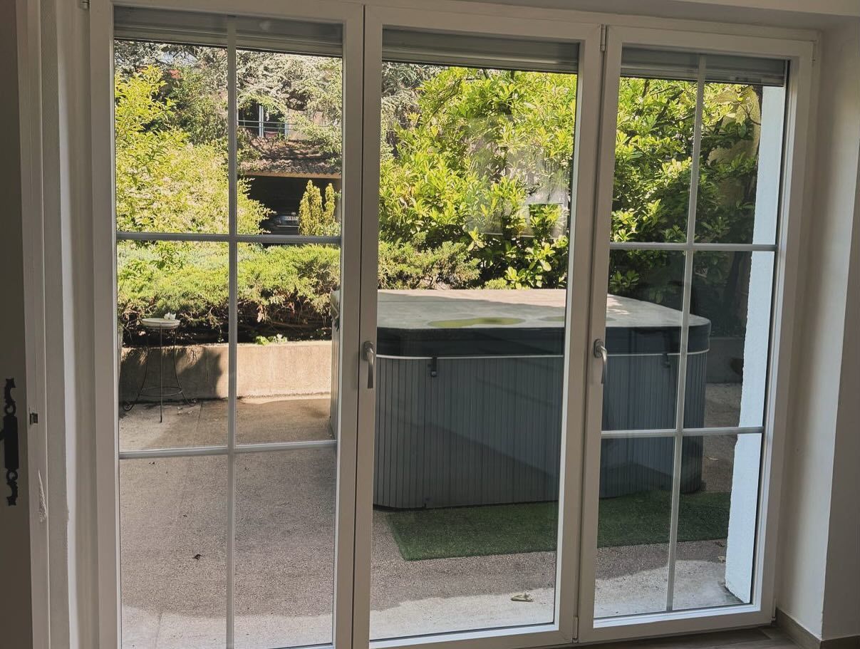 Grandes fenêtres et porte vitrée donnant vers l'extérieur de la maison.