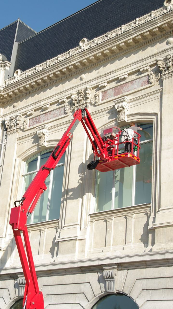 Plan serré d'une nacelle sur laquelle des professionnels lavent les vitres d'un immeuble très haut.