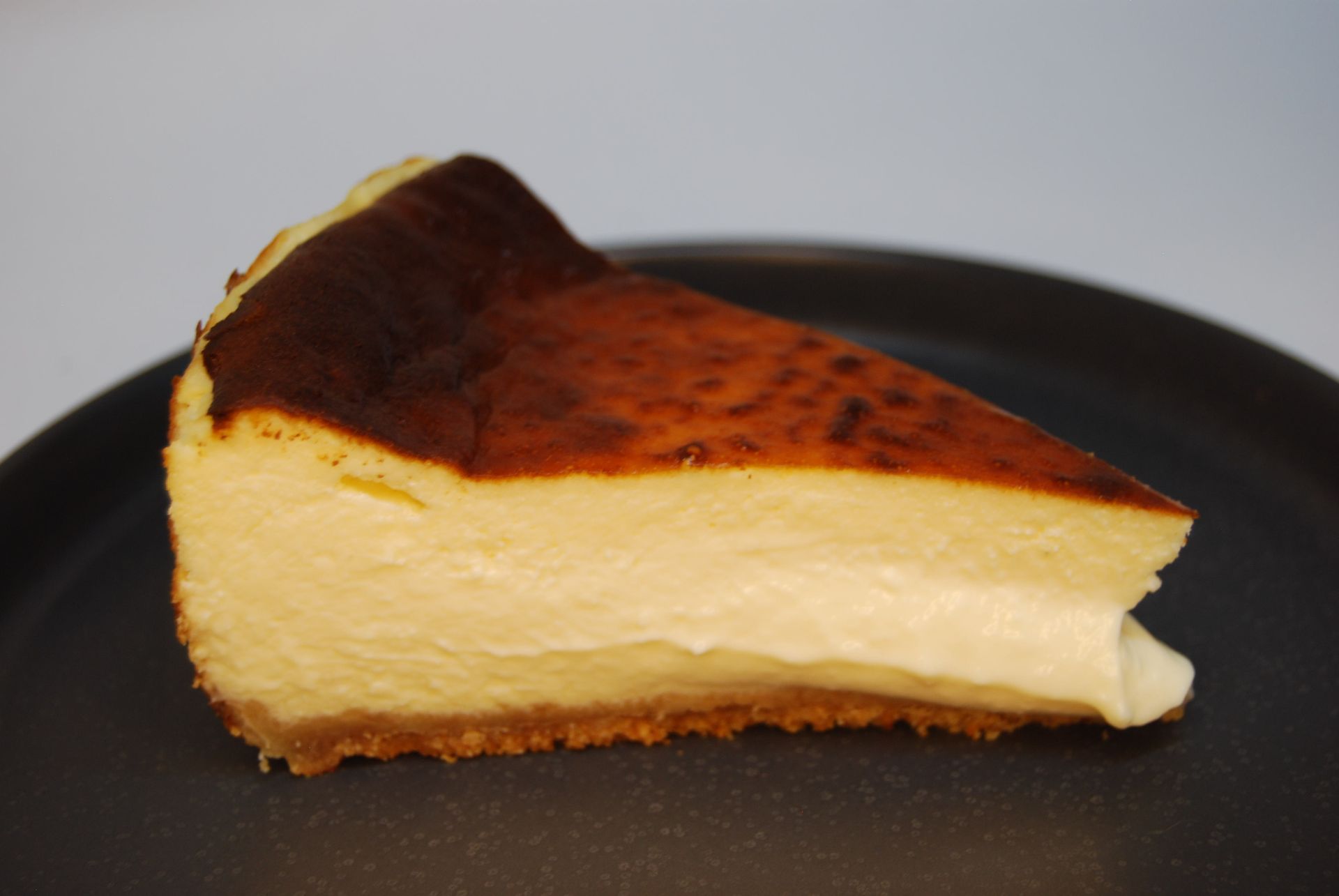 Porción de tarta de queso vasca quemada sobre un plato oscuro, con una superficie caramelizada y un interior cremoso.