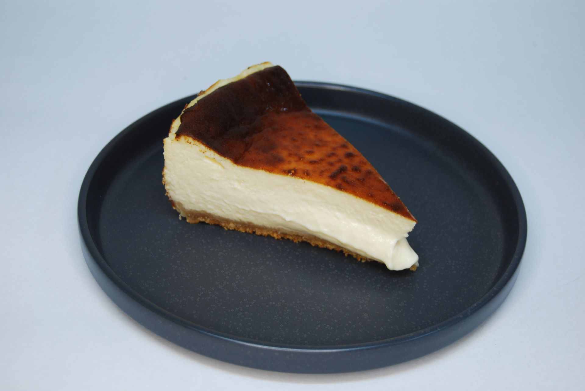 Porción de tarta de queso vasca quemada sobre un plato oscuro, con una superficie caramelizada y una corteza dorada.