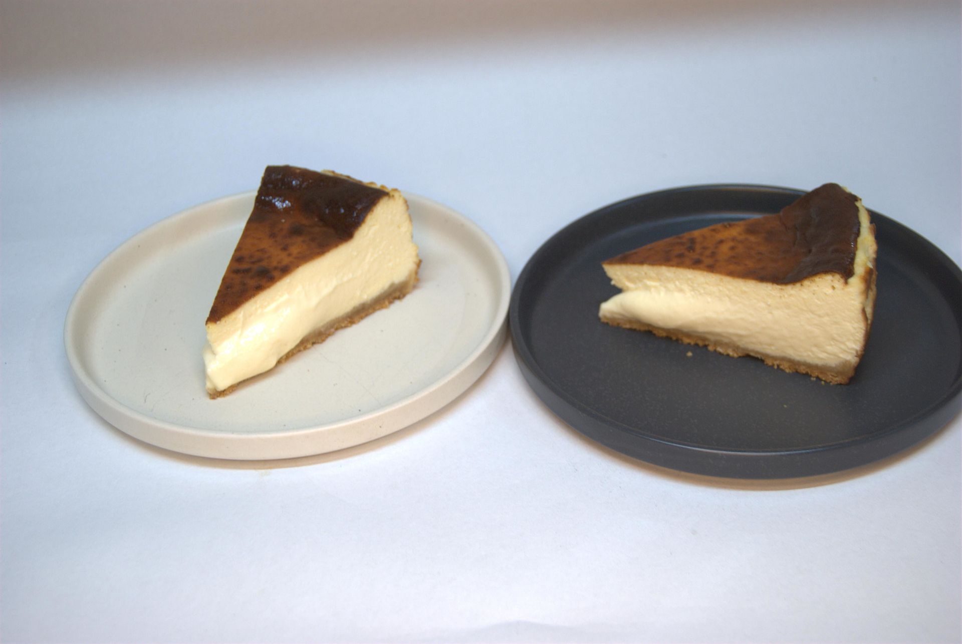 Dos porciones de tarta de queso vasca quemada en platos beige y gris.