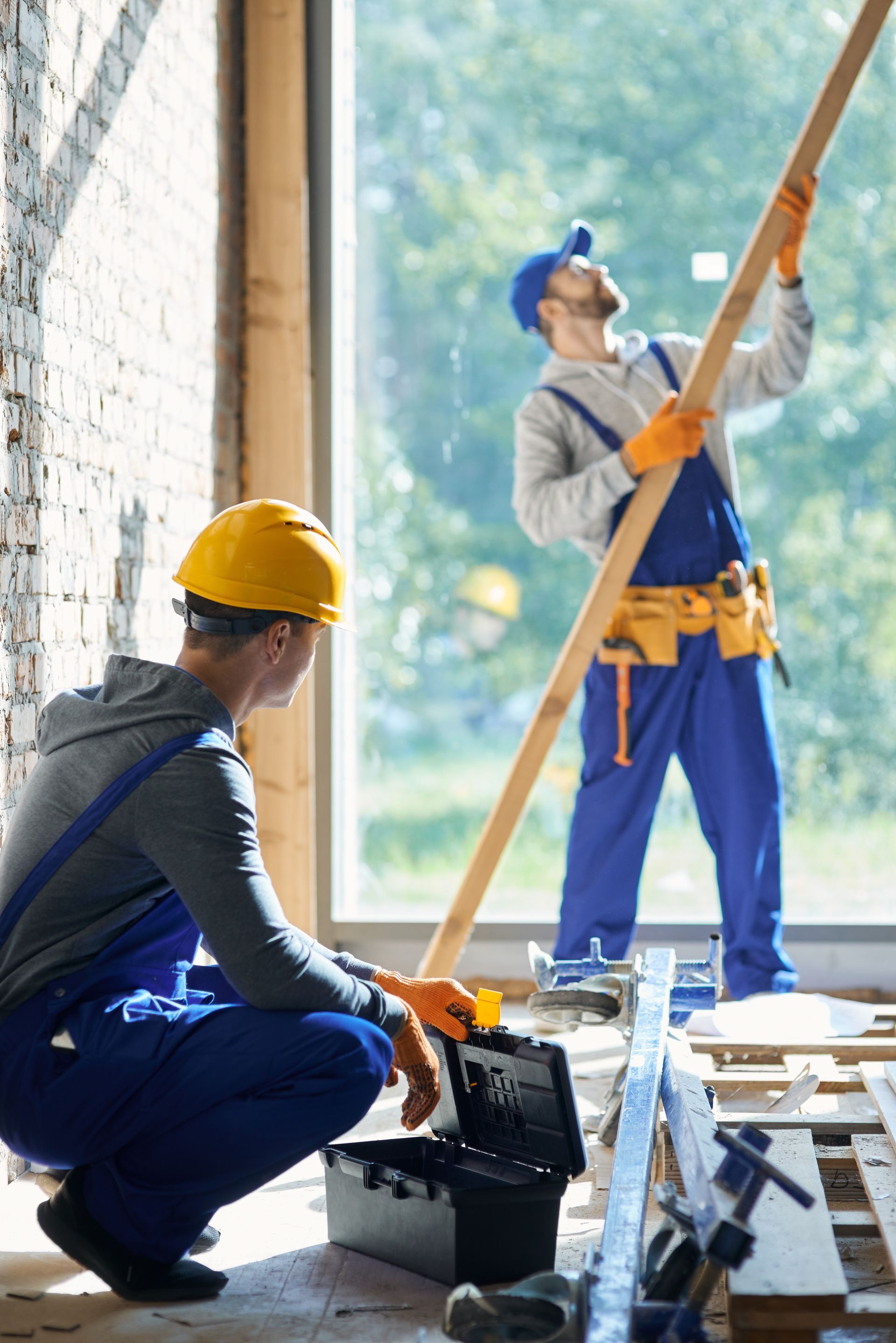 Deux ouvriers installent des poutres en bois sur un chantier. L'un est agenouillé, l'autre tient une poutre.