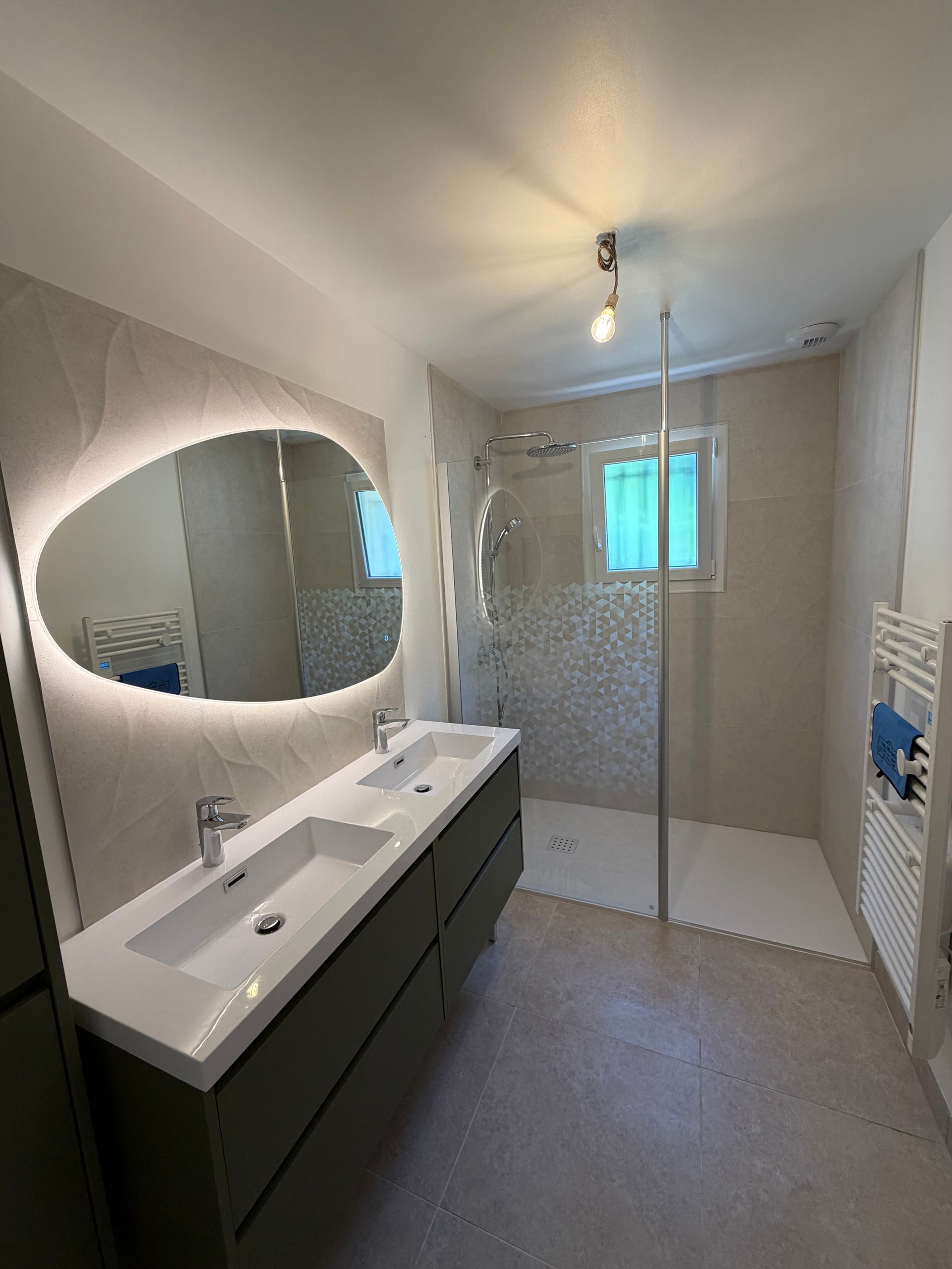 Salle de bains lumineuse avec douche en verre, double vasque, grand miroir et murs carrelés bleus