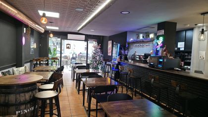 Entrada al bar cafetería “Sabor Urbà” con puertas de cristal, plantas en macetas y un interior oscuro.