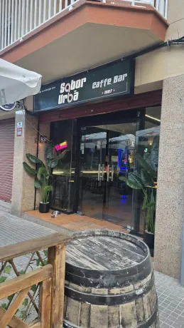 Interior de restaurante con carteles de comida de neón en una pared de madera y plantas; mesa y sillas en primer plano.