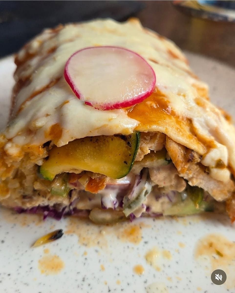 Enchilada cortada a la mitad; pollo, verduras y queso, cubierta con una rodaja de rábano.