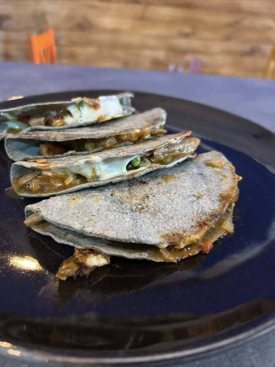 Quesadillas de maíz azul apiladas en un plato azul oscuro, mostrando el relleno y el queso derretido.