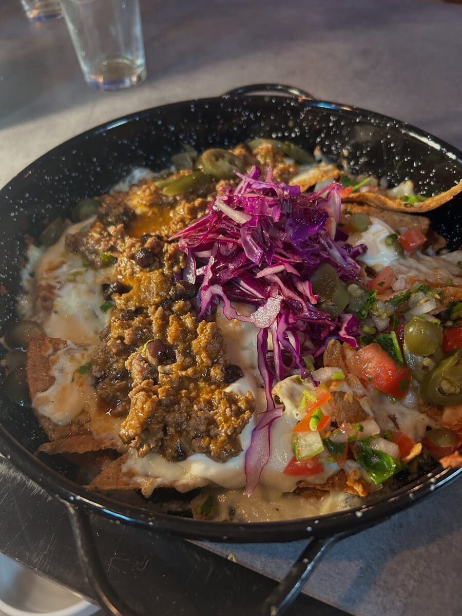 Nachos con carne molida, queso, repollo morado, salsa y jalapeños en una sartén negra.