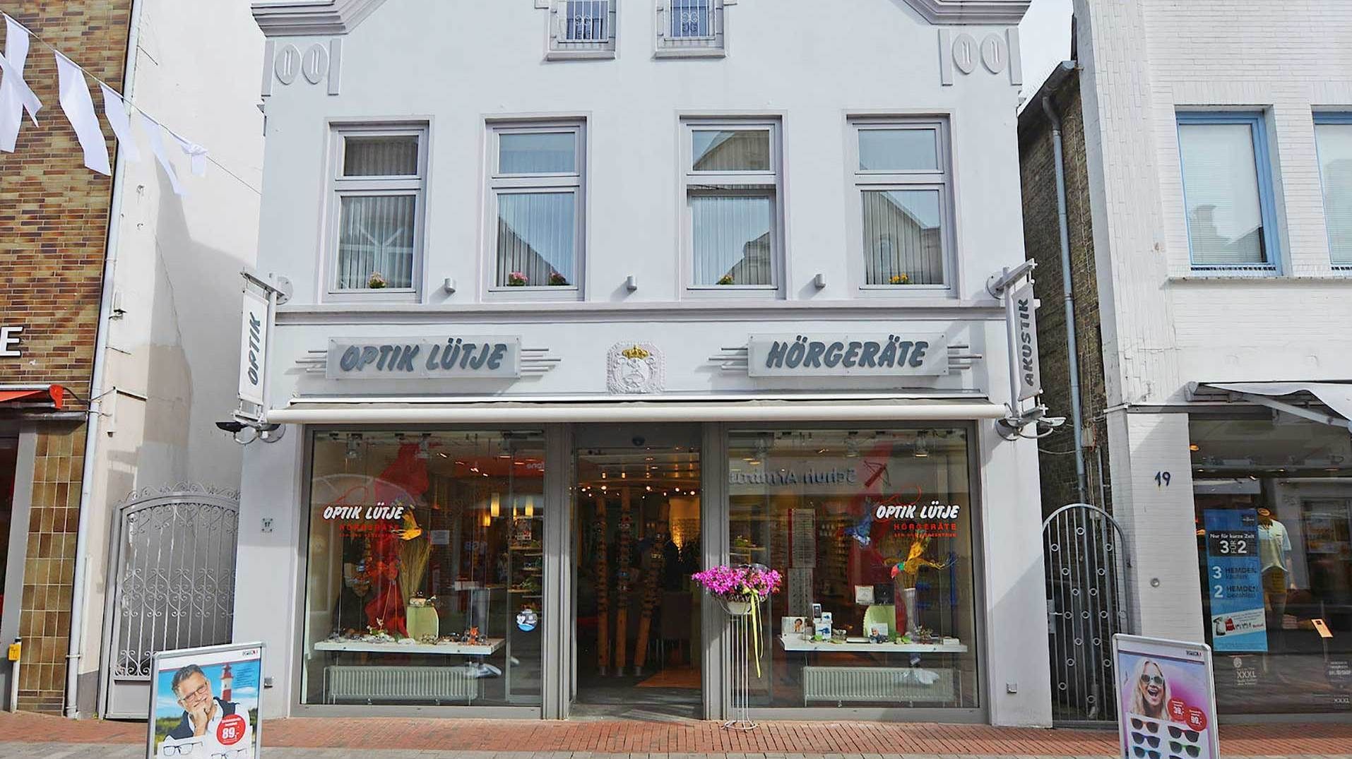 Ein helles, zweistöckiges Gebäude, in dem sich Optik Lütje, ein Optiker- und Hörgerätegeschäft, befindet.