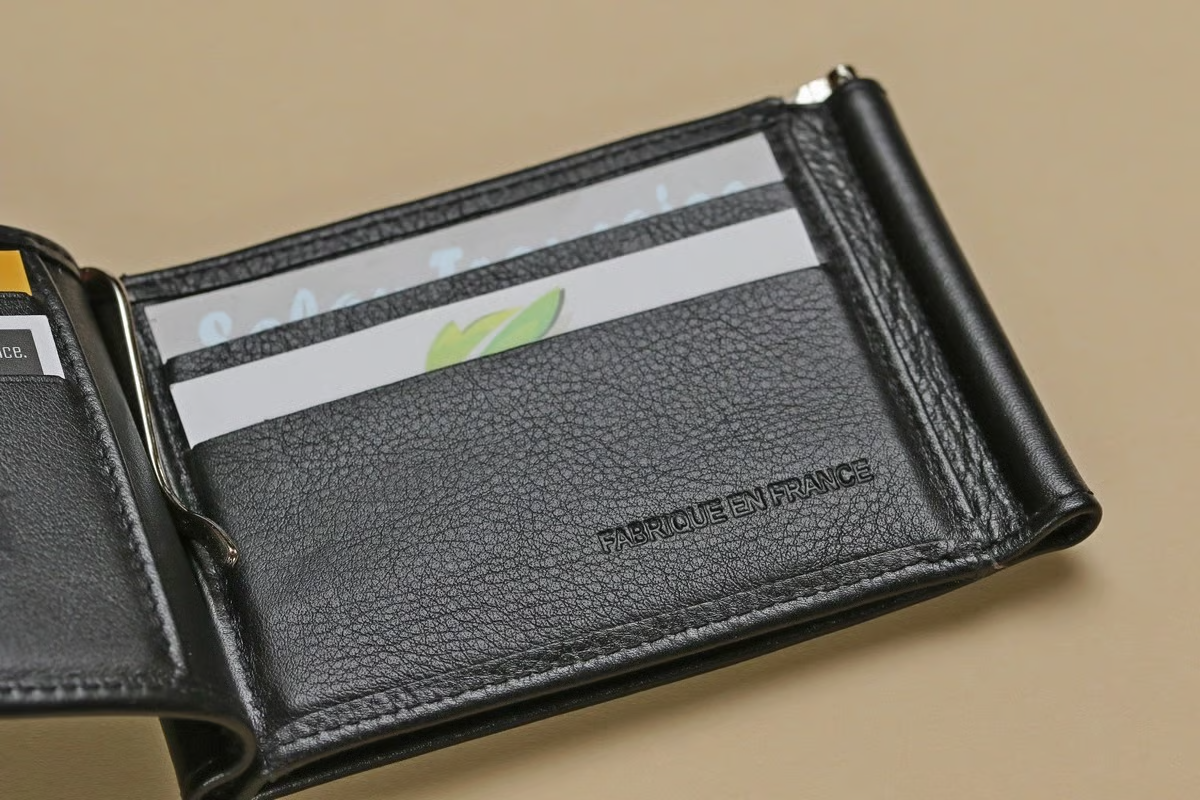 Portefeuille en cuir noir ouvert, pince à billets retenant les cartes de crédit, sur une surface neutre.