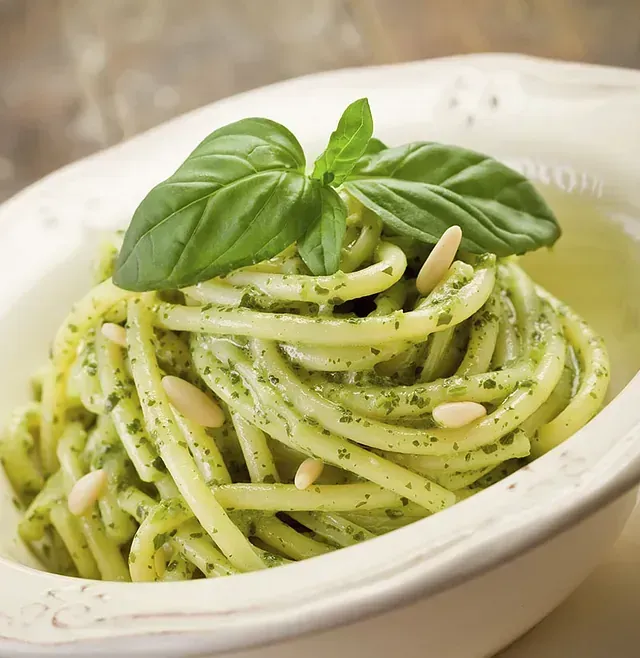 Un tazón de espaguetis con pesto y albahaca encima.