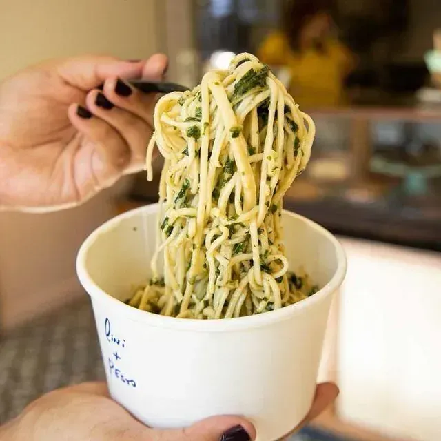 Una persona sostiene una taza de fideos con una cuchara dentro.