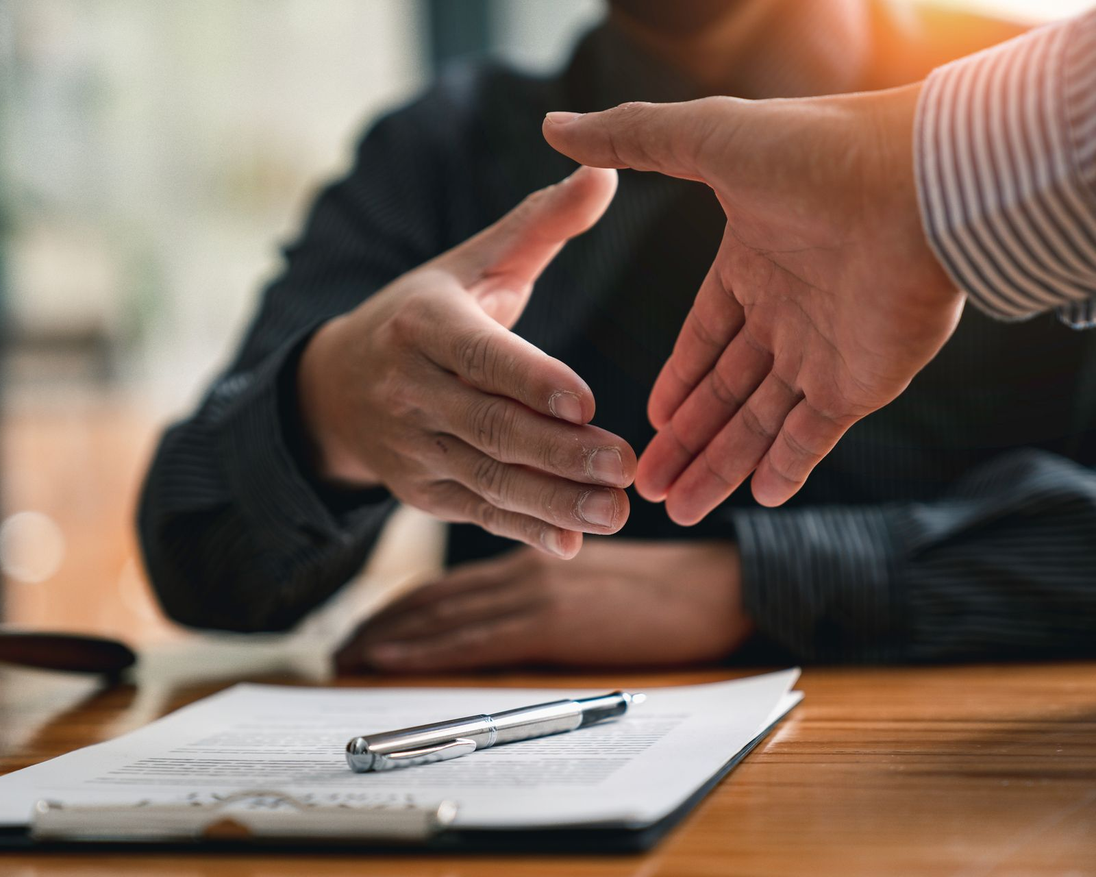 Gros plan sur une poignée de main au dessu d'un document et d'un stylo