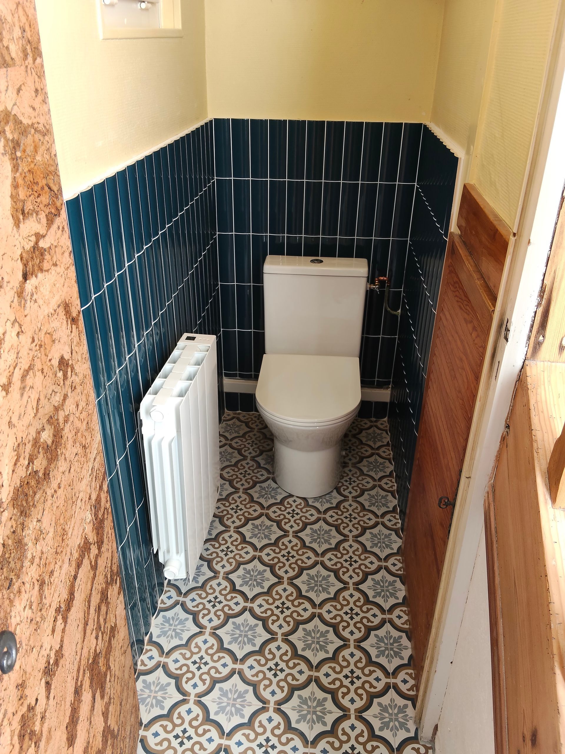 Petite salle de bains avec toilettes, radiateur, carrelage mural et sol.